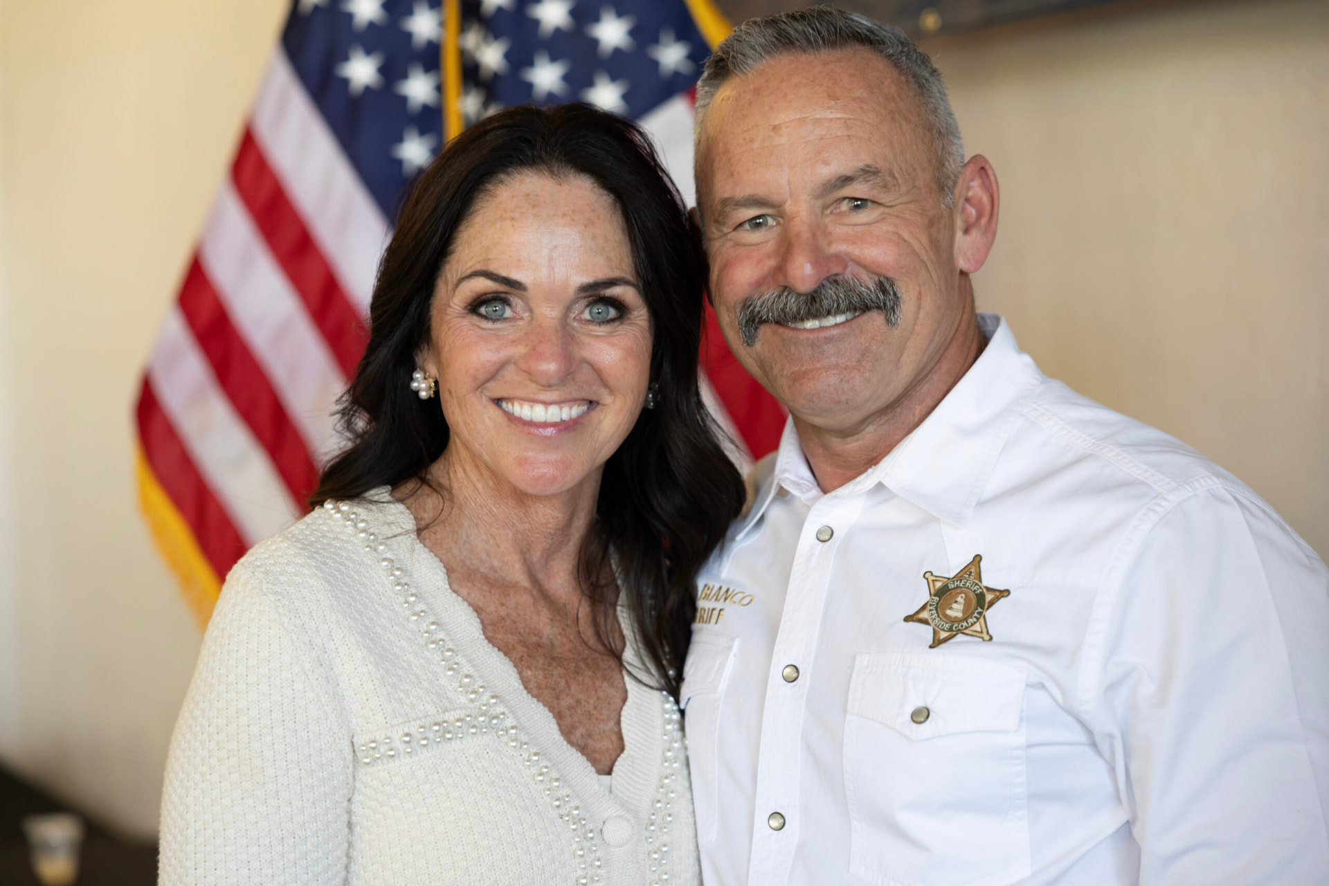 Chad Bianco with his wife in front of the American flag